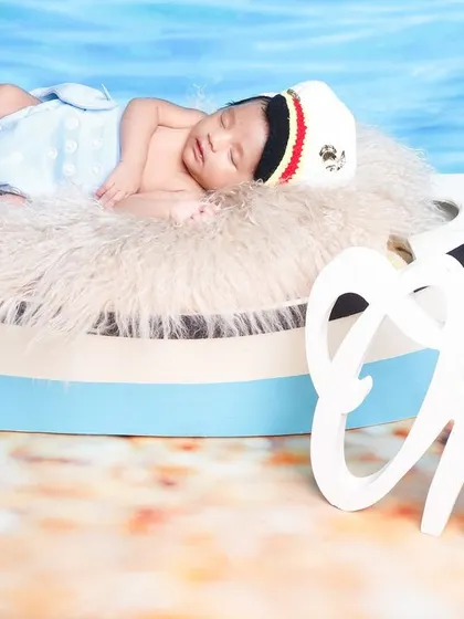 A one-month milestone photo with a nautical theme, featuring the baby sleeping in a boat prop with a "One" sign.