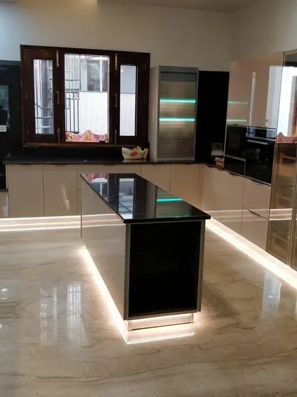 This large U-shaped kitchen features an island with a black granite top. The mirrored and glossy beige cabinets, combined with extensive floor-level lighting, create a glamorous and expansive feel.