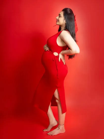 A profile view of a beautiful mom-to-be in a striking red dress. This pose is perfect for showcasing the baby bump against a solid, vibrant background.