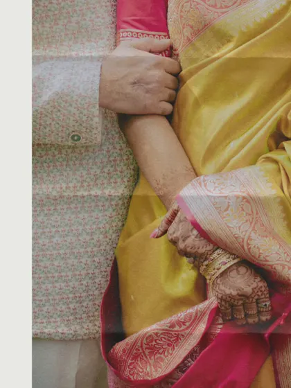 A detailed shot focusing on the texture of the couple's traditional outfits and the way they are holding hands. This photo captures the beauty in the small, intimate details.