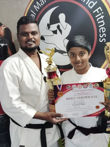 A black belt student with two trophies, showcasing his exceptional performance and achievement in karate.