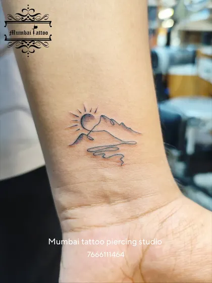 A beautiful minimalist tattoo depicting a sun rising over mountains and a river, all in one continuous line. This design is a testament to our creativity in crafting meaningful landscapes with the simplest of forms.