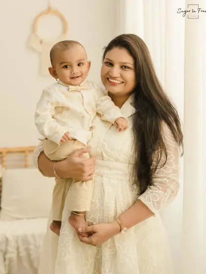 A beautiful mother and son portrait. The mother holds her smiling baby boy, both dressed in light colors that complement the bright and airy feel of the studio.