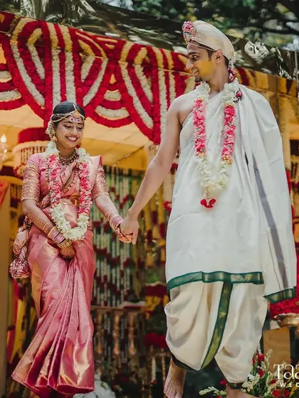 Hand in hand, the newlyweds embark on their journey of forever. This photo captures them walking down the aisle, surrounded by enchanting floral decor that perfectly complements their traditional South Indian wedding attire.