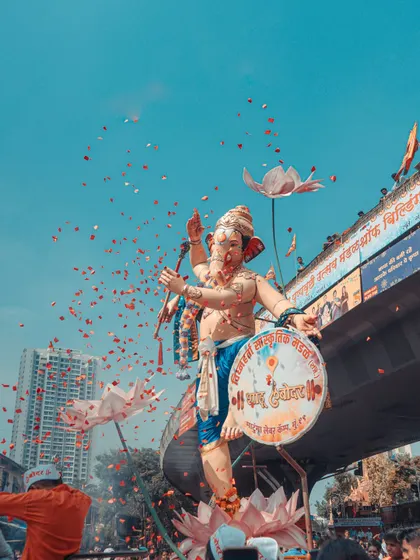 A Ganpati idol against a bright blue sky, with a shower of flower petals. This shot captures the joy and celebratory spirit of the festival.