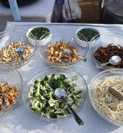 Freshness is key to great food. This image shows the variety of fresh toppings and ingredients we provide for our live stations, including noodles, broccoli, nuts, and fried onions for Khowsuey or pasta.