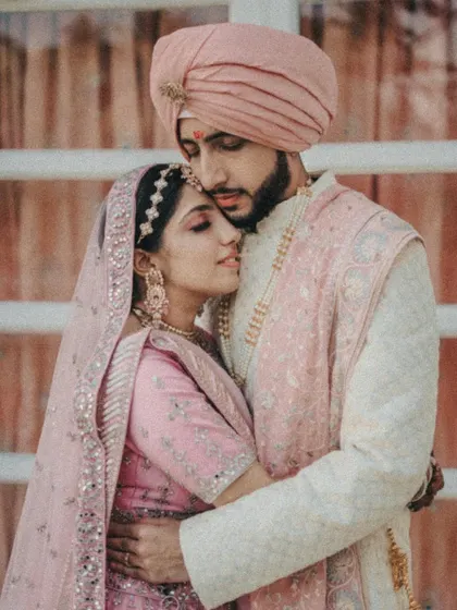 An intimate embrace. This close-up shot captures the couple in a tight hug, their eyes closed, lost in the moment. The soft pink tones of their outfits add to the romance.