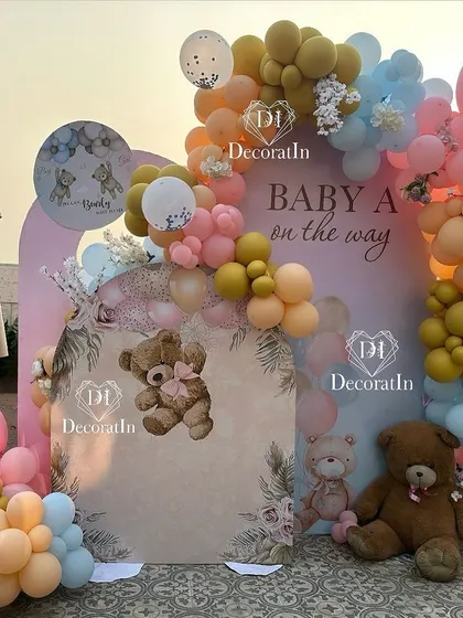 A beautiful outdoor baby shower setup at sunset. The teddy bear theme is brought to life with a custom backdrop, a colorful balloon arch, and cute bear illustrations, creating a warm and inviting scene.