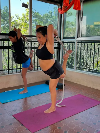 Mother and daughter practicing a strap-assisted standing backbend together. It's wonderful to see family members supporting each other's yoga journey in the studio.