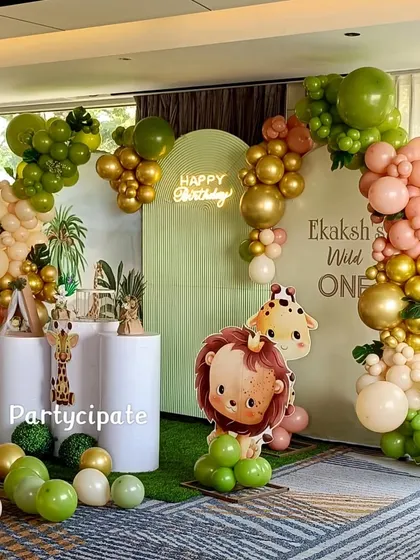 A fun and colorful safari theme for Ekaksh's first birthday. The setup includes a balloon arch in jungle colors, cute animal cutouts, and a 'Happy Birthday' neon sign for a modern touch.