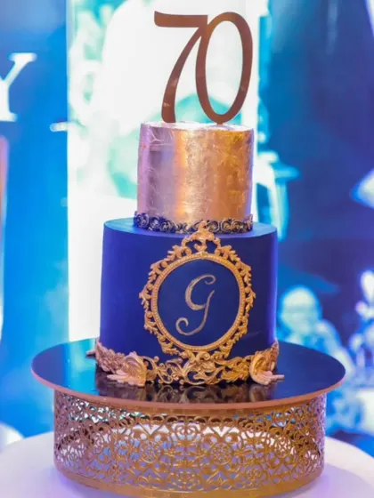 The royal blue and gold 70th birthday cake displayed on a matching gold stand at the event, ready to be the centerpiece of a grand milestone celebration.