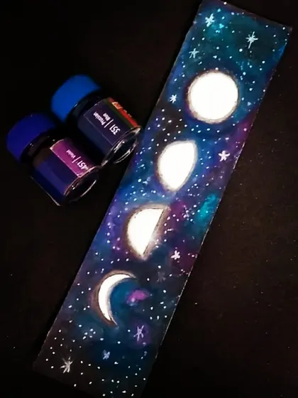 I love making art that you can use every day, like this hand-painted galaxy bookmark. It features the different phases of the moon against a cosmic backdrop of stars and nebulae, created with deep blue and purple inks. It's a small piece of the universe to hold your place in a book.