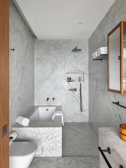 The bathroom in the Worli Duplex is clad in white Carrara marble, creating a serene and monolithic space. The minimal palette is complemented by fluted wood accents, ensuring visual continuity with the rest of the home.