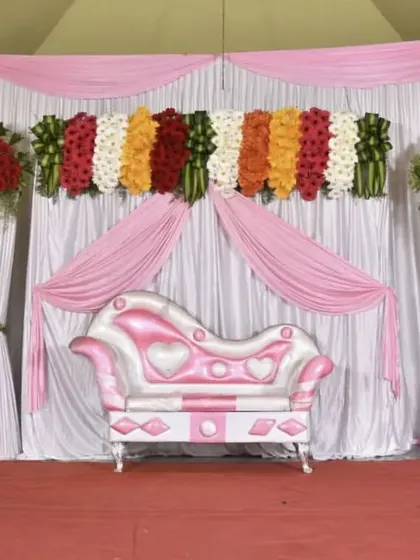 This reception stage uses soft pink and white drapes to create a dreamy atmosphere. The look is completed with large, lush floral arrangements on pedestals, framing the seating area perfectly.