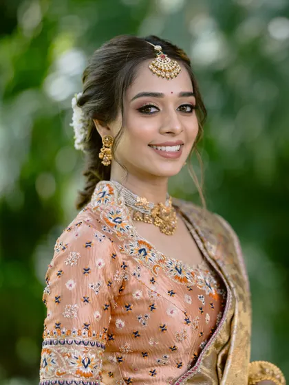 A close-up of the bride's happy face. The makeup is soft and natural, with a focus on enhancing her features and complementing the traditional gold jewellery.