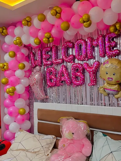A 'Welcome Baby' room decoration with a pink and silver shimmer curtain and a pink, white, and gold balloon arch.