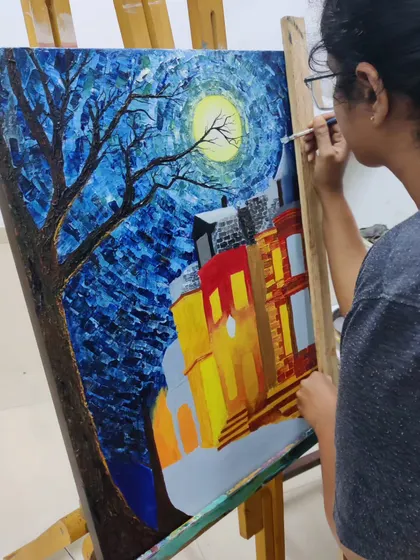 A student works on the sky of her impressionistic night scene, using short, thick strokes to create a sense of movement and energy, inspired by Van Gogh.