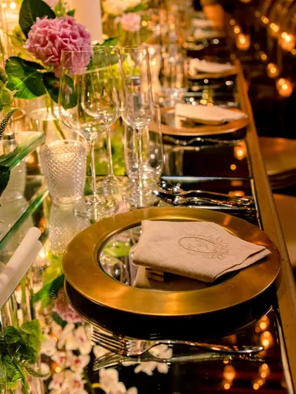 A close-up of a luxurious table setting with gold charger plates and a mirrored surface.