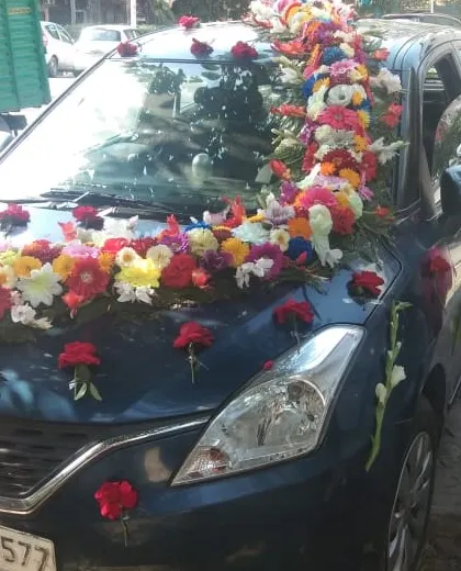 A vibrant and colorful decoration for a blue Maruti Suzuki Baleno. The mix of many different flowers creates a joyful and celebratory look.