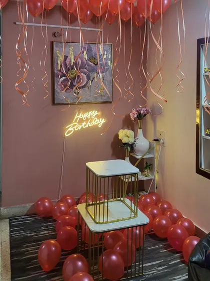 A romantic room decoration with red helium balloons, a neon sign, and balloons scattered on the floor.