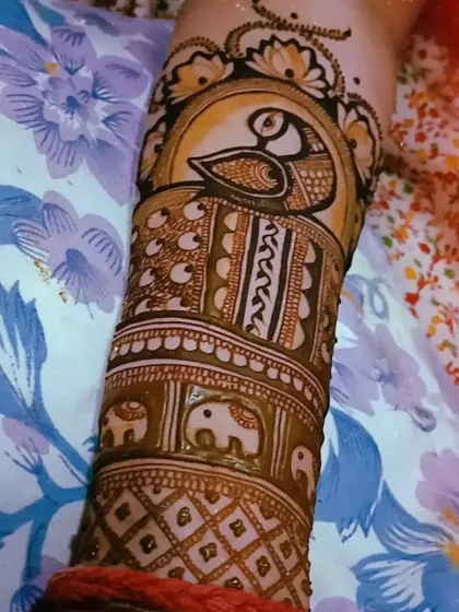 A classic Indian mehendi design on the arm, with a prominent peacock as the main feature, surrounded by bands of elephants and geometric patterns.