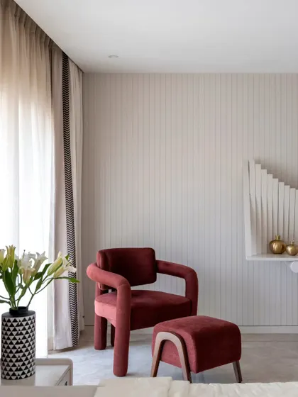 A detail shot from the parent's bedroom, featuring a plush burgundy armchair and ottoman. This cozy reading corner is set against a wall with subtle vertical paneling, adding texture and a sense of height to the room.