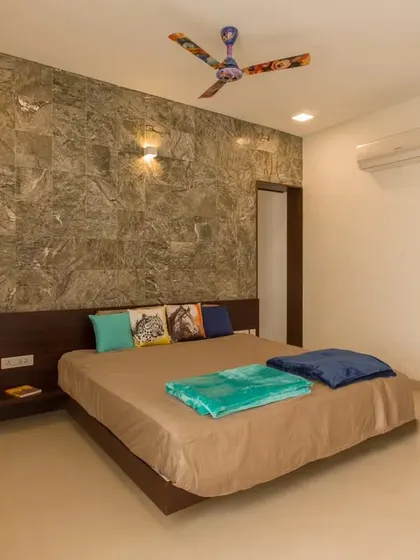 A modern bedroom with a striking green marble accent wall that also serves as a headboard. The room connects to a walk-in closet, showcasing efficient space planning.