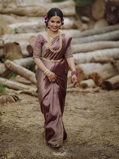 The bride walks with grace and a happy smile, her purple saree shimmering in the light.