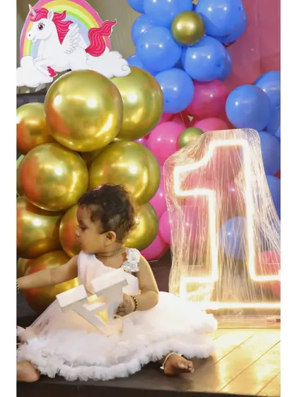 A candid shot of the birthday girl enjoying her unicorn-themed party next to the light-up number '1'.
