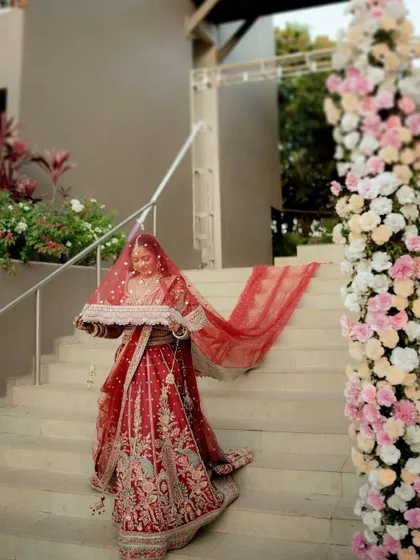 The bride's dramatic entrance down a staircase, her red veil held in a traditional pose.