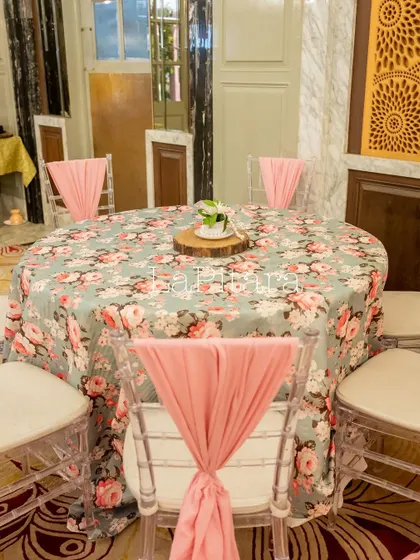 An elegant table setting with a floral tablecloth and pink sashes on the chairs, perfectly matching the tea party theme.