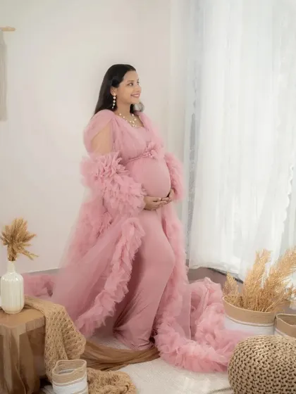 A thoughtful and beautiful portrait of a mom-to-be in a pink gown. She looks out the window in my lifestyle studio, creating a quiet and reflective moment.