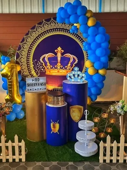A royal prince theme for a first birthday, featuring a large ornate backdrop, a number 1 foil balloon, and a blue and gold color scheme.