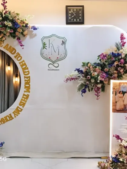 A modern and sophisticated backdrop for an engagement. It features a clean white panel with a circular cutout, a custom couple's monogram, and beautiful floral arrangements.