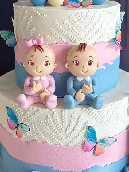 A stunning three-tiered gender reveal cake. The design features adorable fondant babies in pink and blue, surrounded by delicate butterflies.
