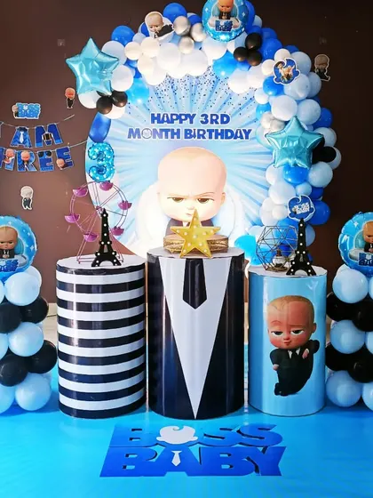 A cute Boss Baby setup for a 3-month birthday celebration. The decor features a backdrop with the baby's picture, themed pedestals, and blue and black balloon pillars.