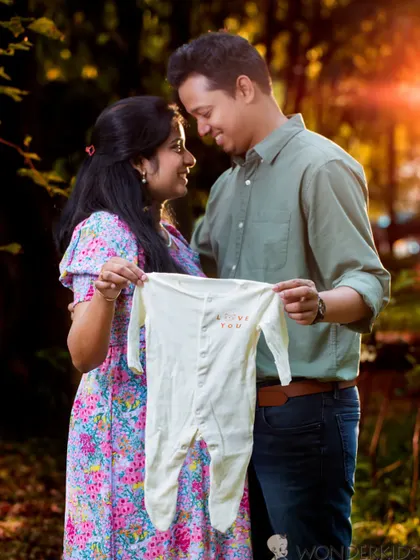 Holding up a tiny baby onesie is a classic and heartwarming way to announce your excitement. This photo captures that joyful anticipation during a golden hour outdoor session.