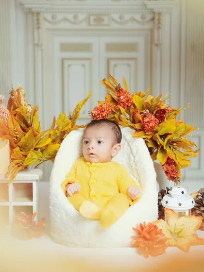 This newborn is sitting comfortably in a soft chair, surrounded by warm autumn colors. I have a variety of props to match any season or theme.