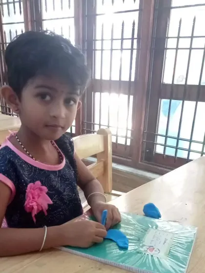 A young girl uses a tool to shape her blue clay, fully engaged in her project. We provide various tools to help children explore different techniques in their art.