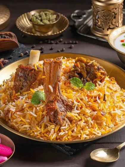A rich Mutton Biryani with bone-in pieces, garnished with fresh mint and served with raita and pickled onions.
