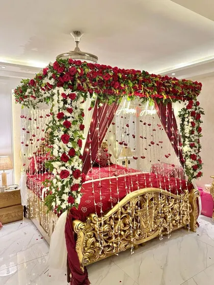 A truly royal wedding night decoration. The ornate golden bed is decorated with a canopy of red and white roses and hanging floral strings.