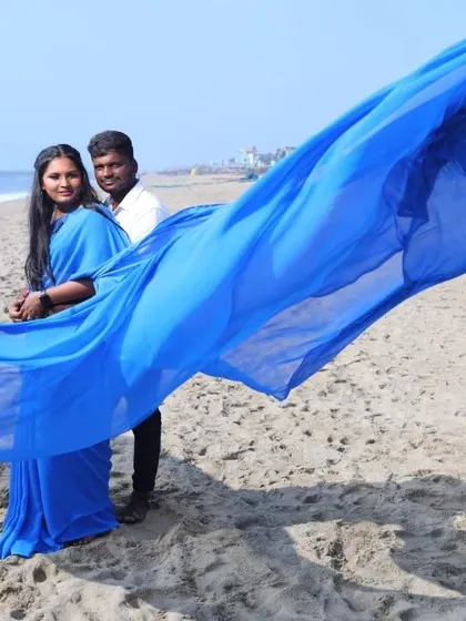 The wind catches the trail of the blue flying saree, creating a stunning, dynamic shot against the ocean backdrop.