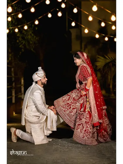 A playful and romantic moment as the groom kneels to help his bride, with fairy lights creating a magical background.