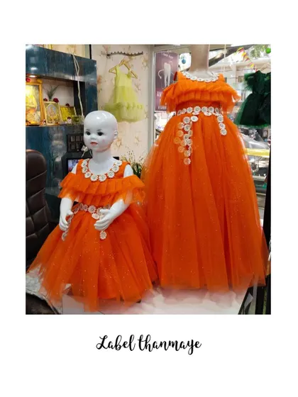 Another view of the orange twinning gowns, showing the off-shoulder design and ruffled neckline.