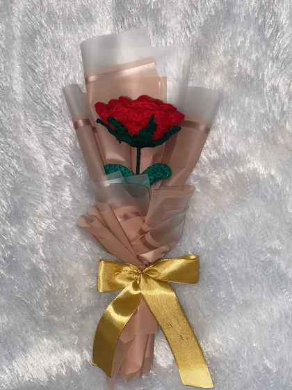 A flat lay of the single red rose bouquet against a soft white background, highlighting its delicate wrapping and rich color.