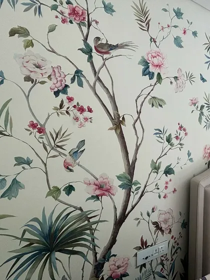 A bedroom sanctuary is created with this hand-painted Chinoiserie wallpaper. The design features delicate birds perched on blossoming branches, offering a unique blend of color, texture, and artistry that elevates the entire room.