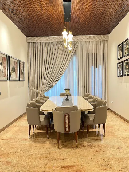 A full view of the 10-seater dining space, showcasing the harmony between the furniture, the warm wooden ceiling, and the soft, floor-to-ceiling curtains that frame the room.