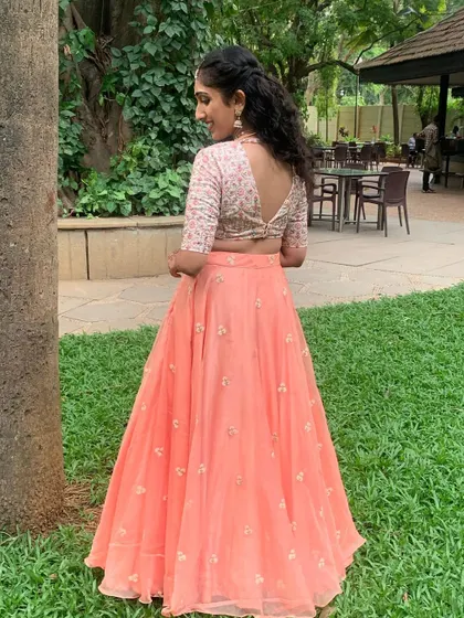 A closer look at the back of this peach Sangeet lehenga. The V-neck blouse is fully embroidered, and the flowing organza skirt is detailed with small, scattered floral motifs for a romantic feel.