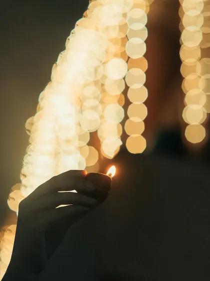 A hand holding a diya, with a background of beautiful bokeh from the festive lights. This shot plays with light and shadow to create a classic, artistic Diwali portrait.