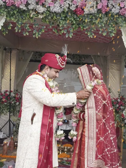 A couple during their Jaimala ceremony under a beautifully decorated mandap. The floral canopy and drapes create a vibrant yet elegant space for the wedding rituals to unfold.